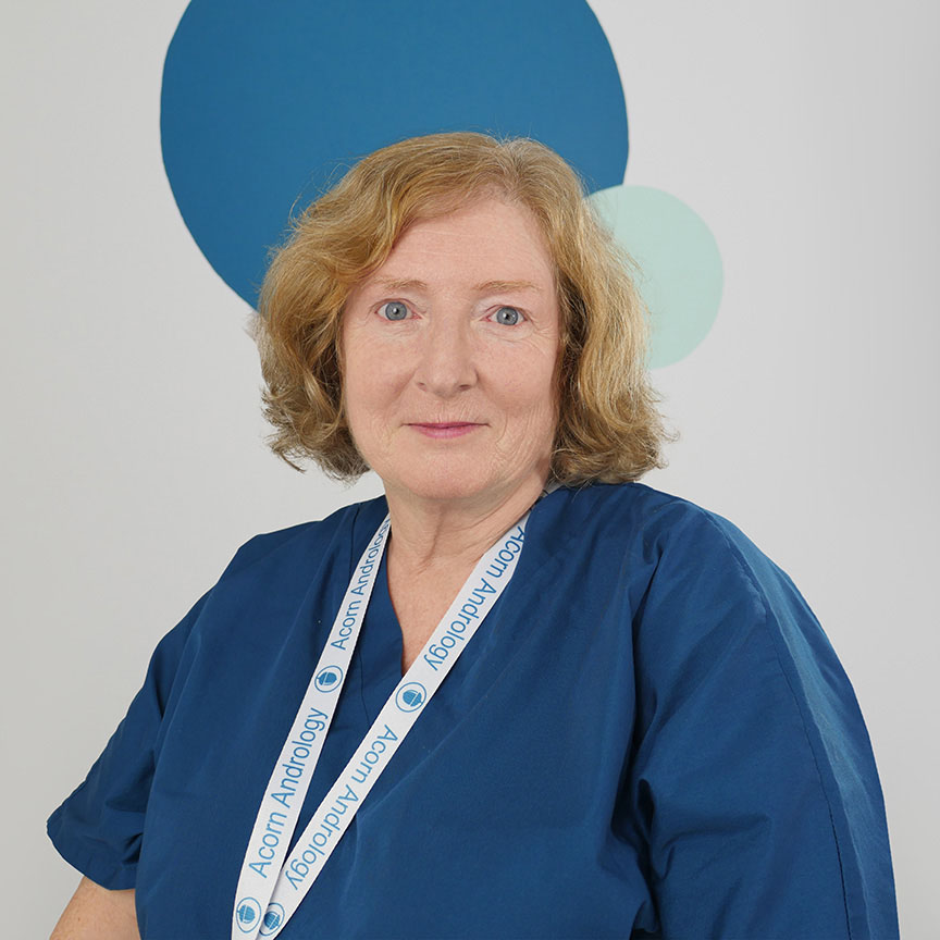 This image features Ecem, a Lab Technician at Acorn Andrology, wearing a blue medical uniform and an Acorn Andrology lanyard. She has long, dark hair that falls over her shoulders, and she stands against a backdrop of abstract circular patterns in blue and teal tones. Ecem plays an important role in supporting laboratory work related to male fertility treatments, ensuring high standards of patient care and laboratory analysis.